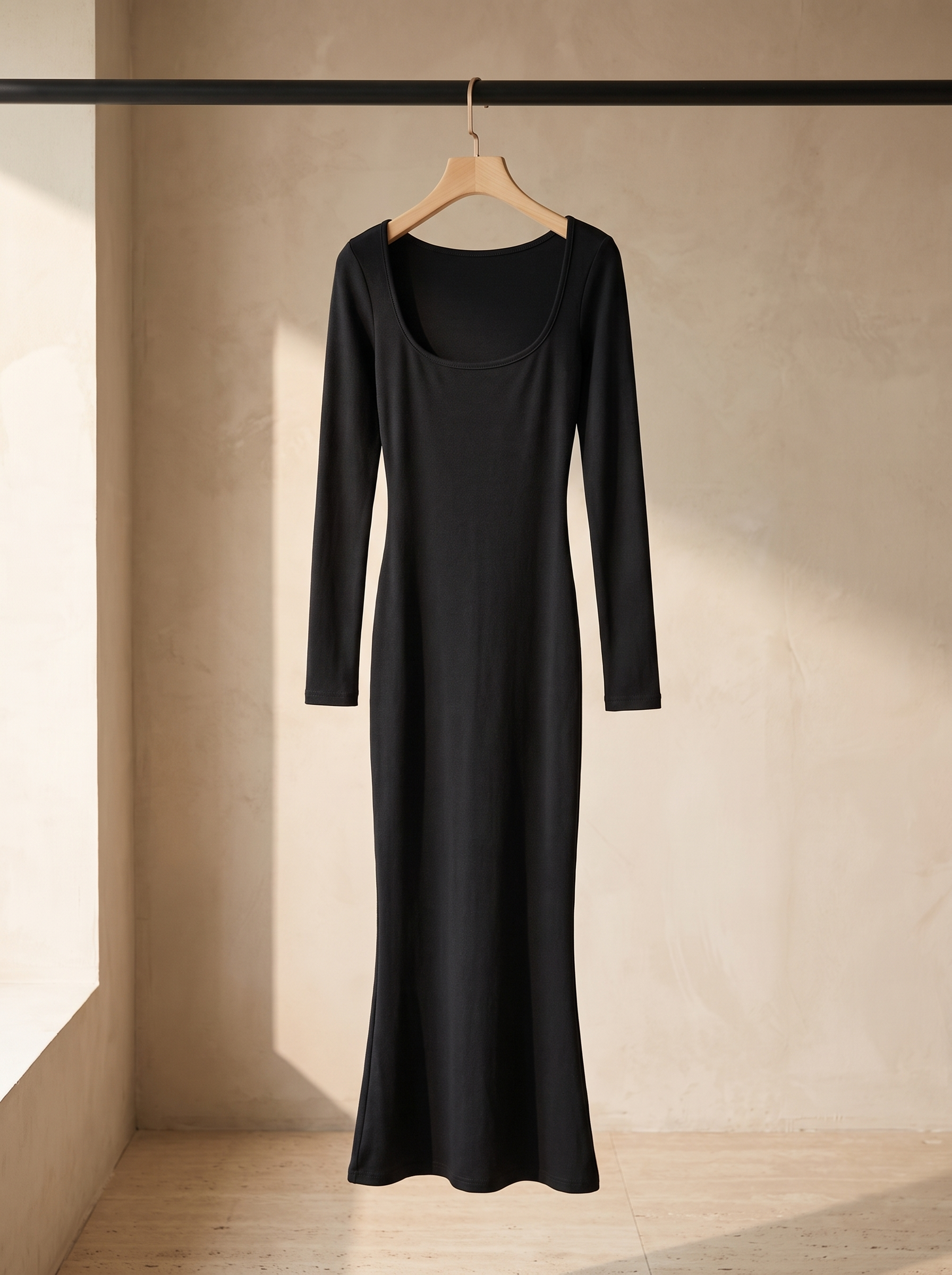 Vestido Esencia negro colgado en percha de madera sobre pared de microcemento